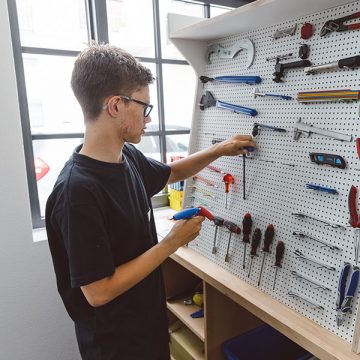 Ein junger Mitarbeitender bei FahrRad R18 sucht Werkzeug von einer Werkzeugwand.