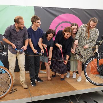 Sechs festlich und leger gekleidete Menschen stehen auf der Bühne und durchtrennen mit Kneifzangen ein Absperrband aus Fahrradketten-Gliedern - Eröffnungszeremonie von FahrRad R18