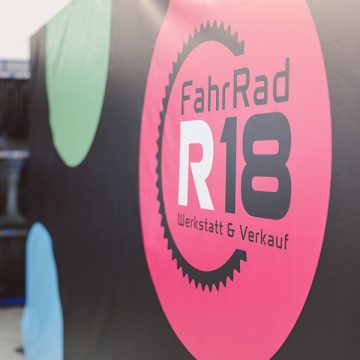 Logo von FahrRad R18, aufgedruckt auf einer Bannerplane, die im Ladengeschäft der Münchner Werkstatt hängt.