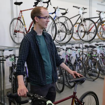 Fahrradservice-Ansprechpartner Jan Llaleike steht mit rotem Rennrad vor weiteren Fahrrädern. Er lächelt und hält das Bike leger mit beiden Händen.