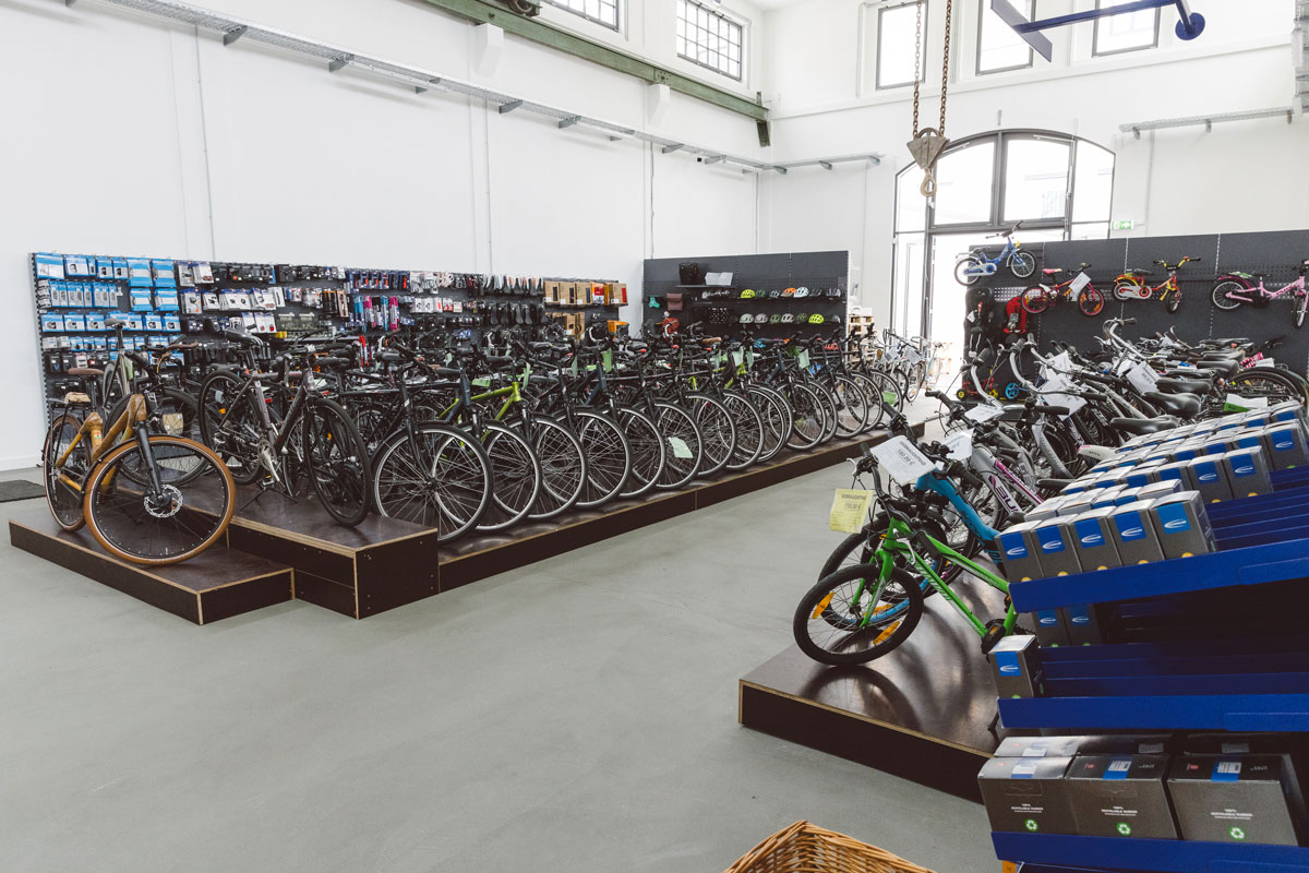 Die Neuräder-Ausstellung des Ladengeschäfts FahrRad R18 in München. Zu sehen sind schön geordnete Fahrräder in allen Farben, in einer Ausstellungshalle (weiße Wände)